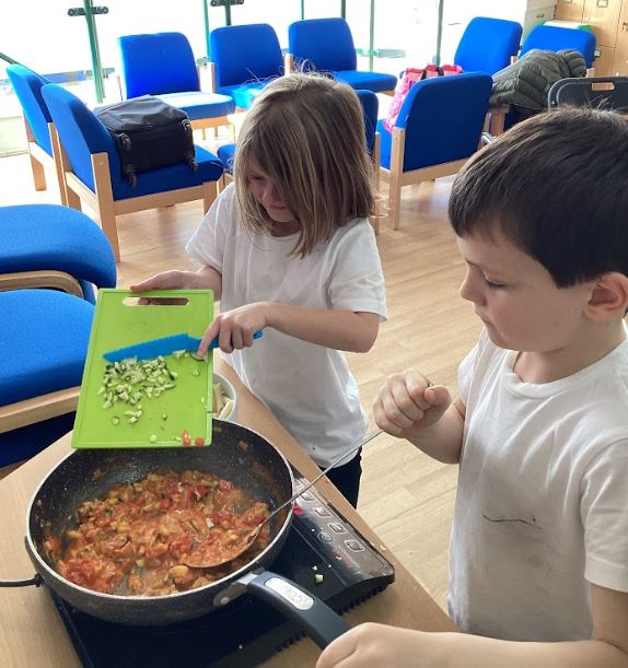 Two children adding ingredients into a frying pan.