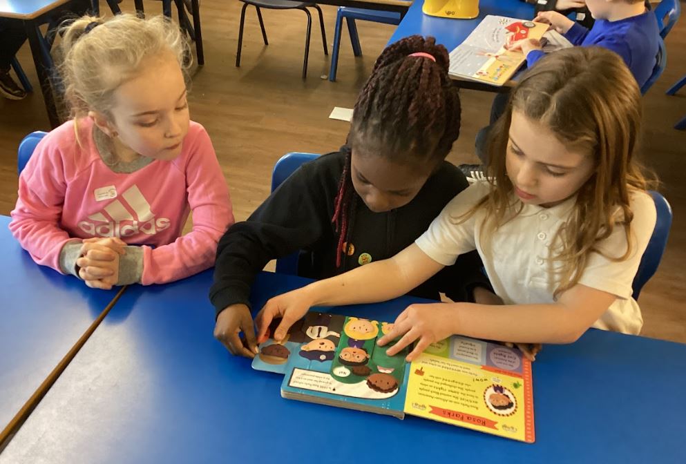 Three children looking at a book and sliding a compartment out from the side to see what is underneath.